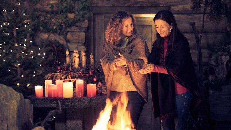 Adventzauber im Waldviertel, © Andreas Hofer Photography Zwei Frauen stehen lächelnd an einem Feuer, umgeben von Kerzen und Weihnachtsdekoration.