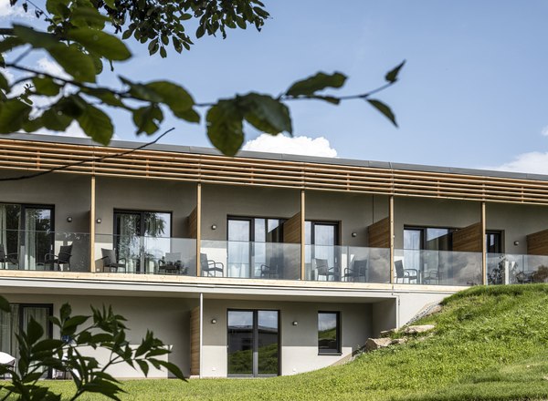 Hotel Ottenstein, © C&G Gastgewerbe GmbH Modernes zweistöckiges Gebäude mit Glasbalkonen und Holzverkleidung, umgeben von grüner Landschaft.