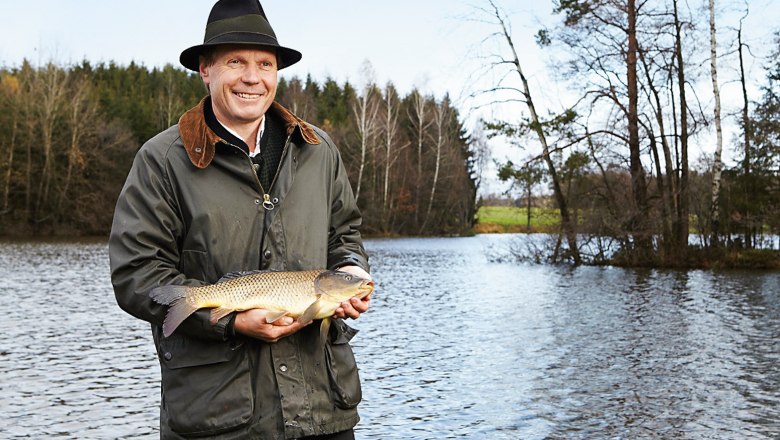Karpfenteich, © Waldviertel Tourismus/Thomas Topf Mann mit Hut hält einen Karpfen vor einem Teich.