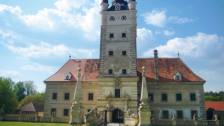 Schloss Greillenstein mit Turm und roten D&auml;chern, umgeben von Statuen und einem Tor.