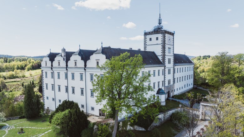 Schloss Weitra mit Garten und Turm, umgeben von Bäumen und Landschaft.