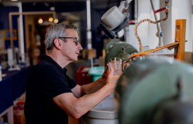 Ein Mann bearbeitet ein Kristallglas an einer Schleifmaschine in einer Werkstatt.