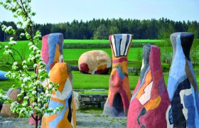 Bunte Skulpturen in einer gr&uuml;nen Landschaft mit B&auml;umen im Hintergrund.