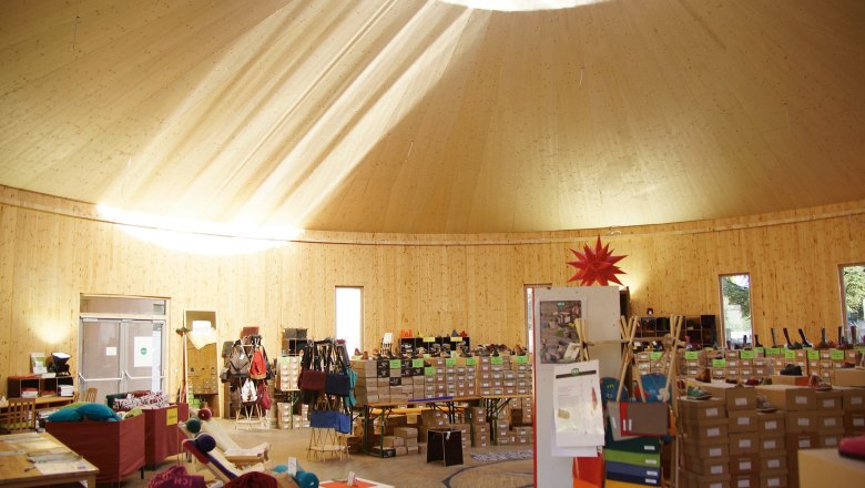 Innenansicht einer Holzjurte mit Verkaufsst&auml;nden und Sonnenstrahlen durch das Dachfenster.