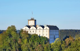 Schloss Weitra auf einem bewaldeten H&uuml;gel vor blauem Himmel.