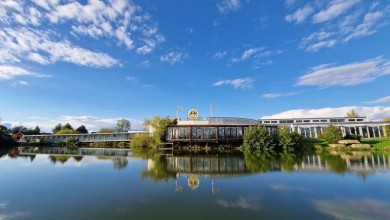 Außenansicht der Käsemacherwelt mit blauem Himmel und See im Vordergrund.