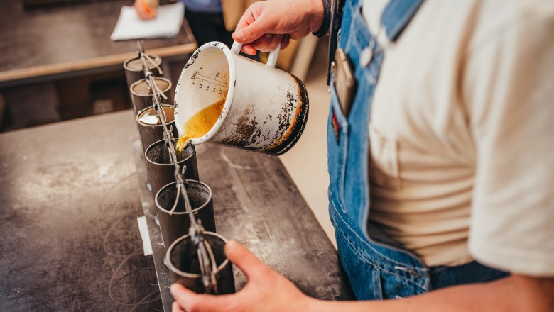 Person gie&szlig;t fl&uuml;ssiges Wachs in Kerzenformen.
