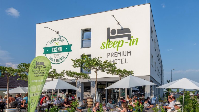 Außenansicht des Sleep-in Premium Hotels mit Restaurant Egino und Terrasse.