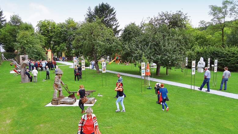Menschen im Karikaturengarten Brunn am Wald mit Skulpturen und Bäumen.